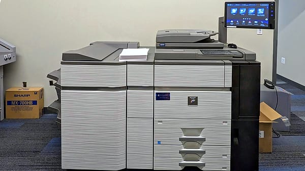 A large office photocopier standing against a wall with its output tray open