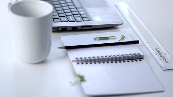 A steel ruler lying on a desk beside a closed laptop and a small notebook