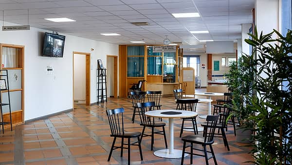 A public reception area with round tables and chairs and a corridor leading off it