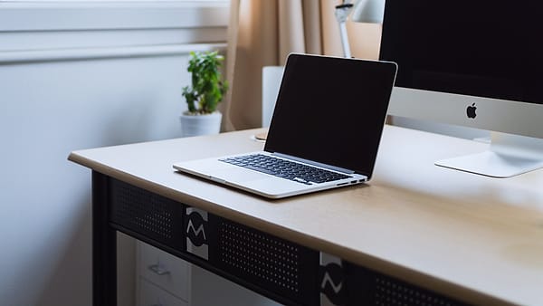 An open laptop on a tidy desk beside a notebook, lit by daylight from one side