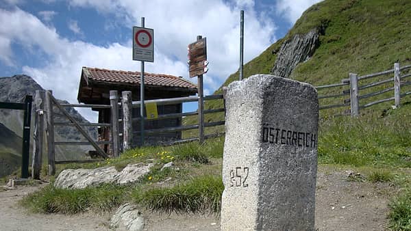 A border marker and a disused checkpoint post standing together on a mountain pass