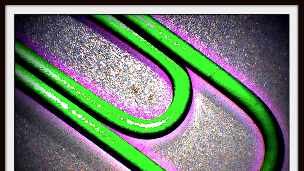 A single metal paper clip photographed in close-up against a plain pale background