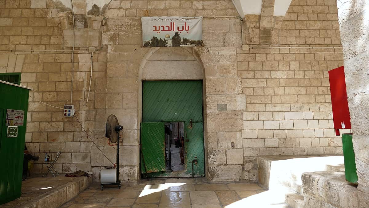 A closed iron gate set into a stone wall, its bars throwing shadows across the ground